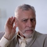 older man trying to hear better with his hand