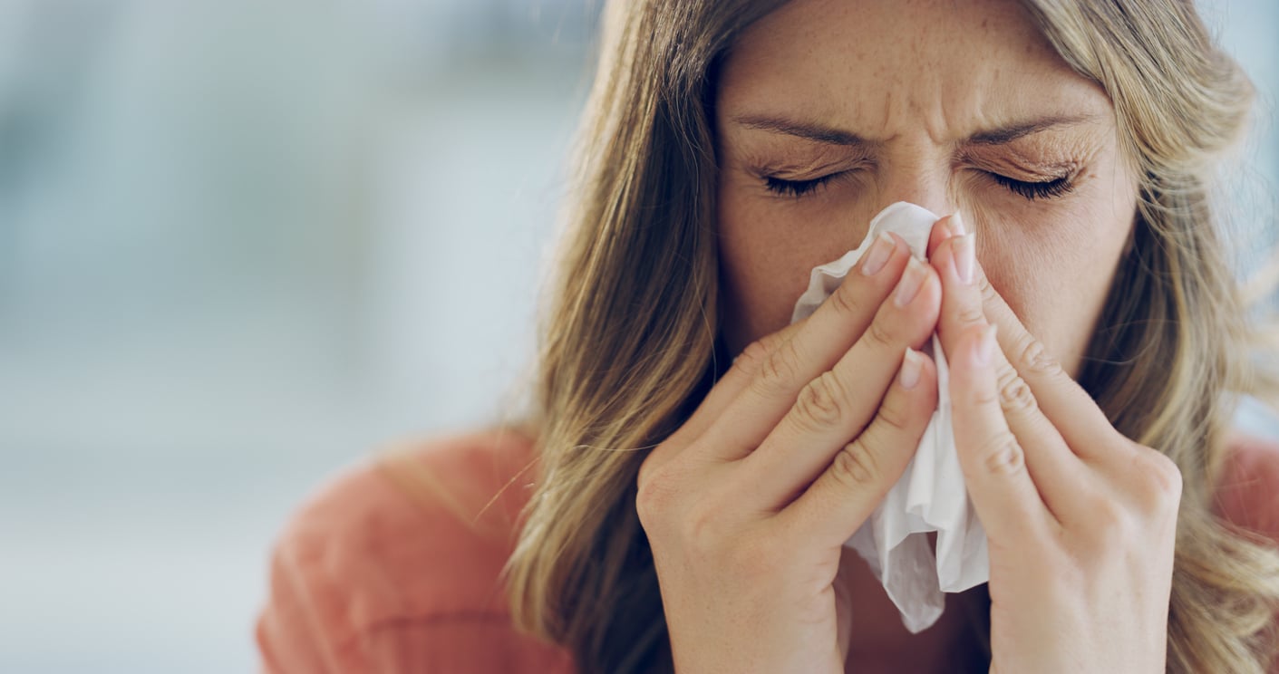 close up of woman blowing nose with blurry background