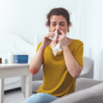 woman sitting on couch while using nasal spray for her runny nose