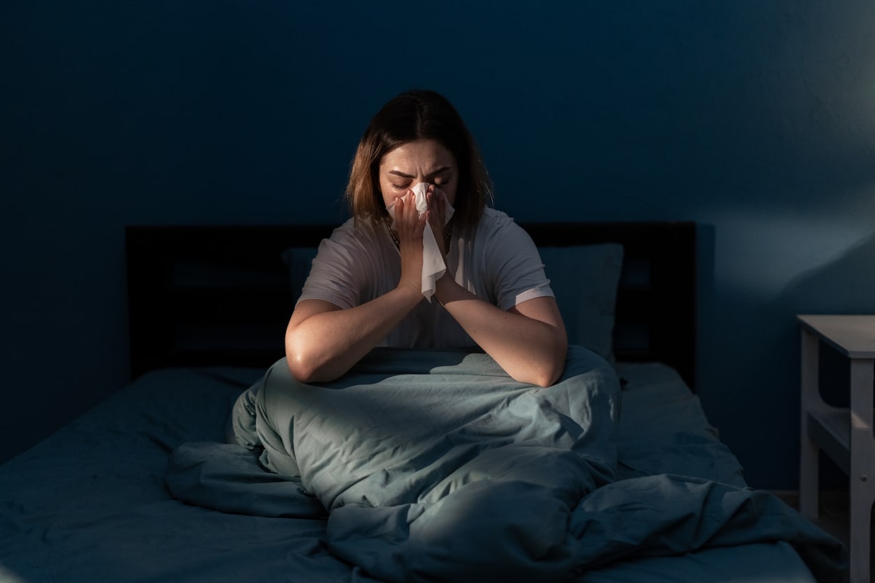 Beautiful woman suffering cold and flu trying to sleep at night, girl sneezing into a tissue in bedroom. Illness colds or flu. Allergy or health issue concept.