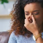 Headache, woman and living room sofa with anxiety and stress from burnout and allergies. Home, sick and illness of a female person with nasal congestion and sinus pain on couch with frown and disease